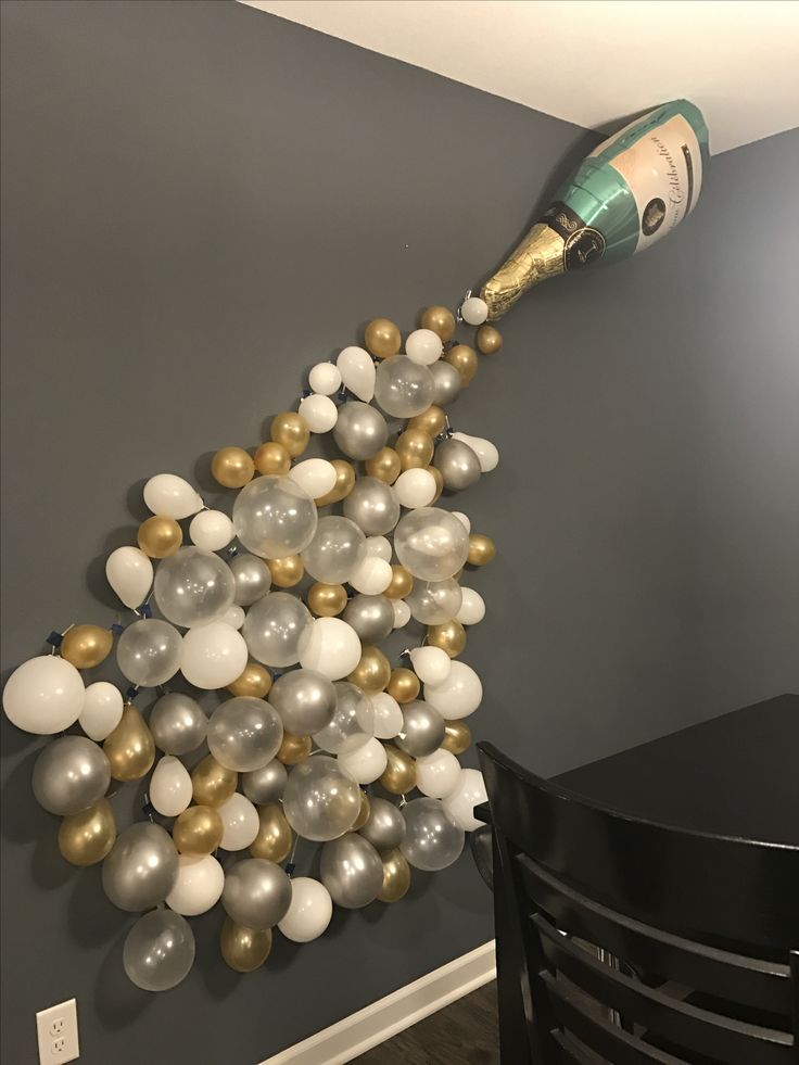 a party decoration with champagne bottle and white and gold balloons on the wall in a dining room