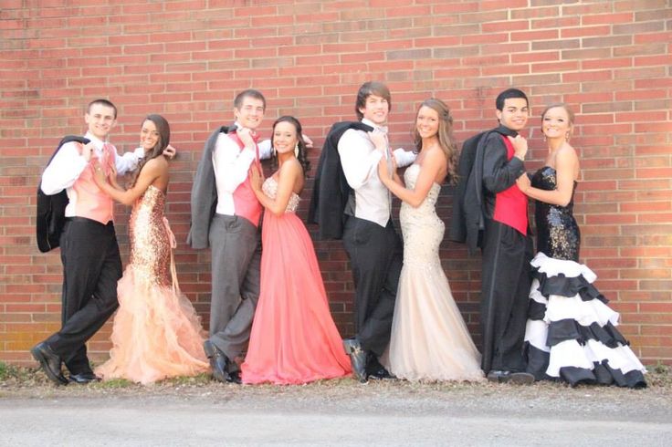 a group of people standing next to each other in front of a brick wall wearing formal clothing