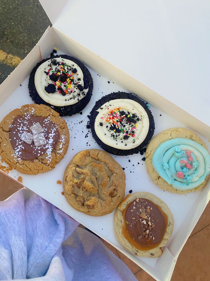 an open box of cookies with frosting and sprinkles on them, sitting on a table