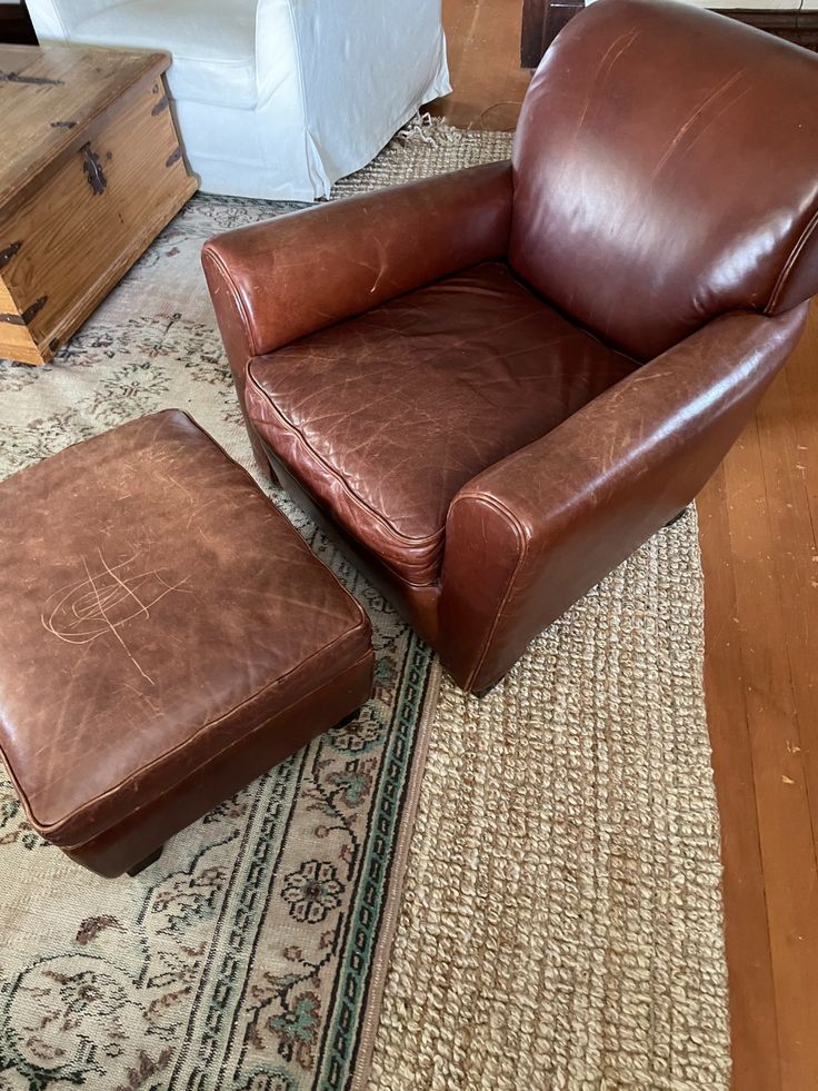 a brown leather chair and foot stool in a living room with a rug on the floor