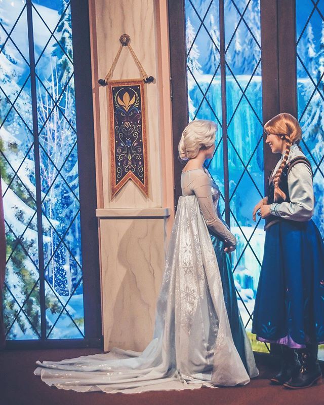 two children dressed as frozen princesses standing in front of a stained glass window looking at each other