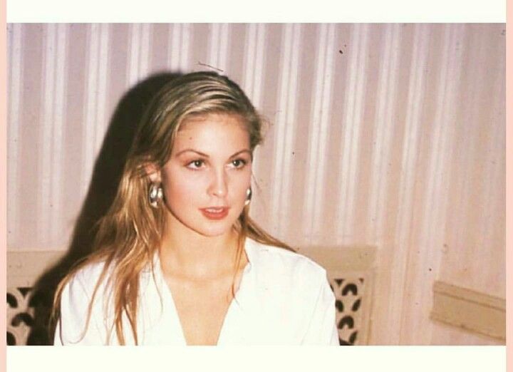 a woman with long hair and earrings sitting on a couch in front of a wall