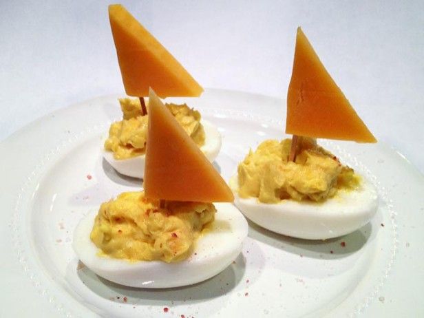 deviled eggs topped with cheese and cheddar wedges on a white plate