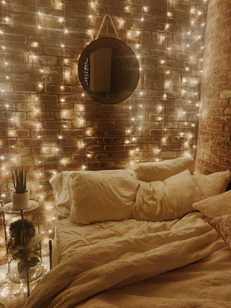 a bedroom with lights on the brick wall and white bedding, pillows and blankets