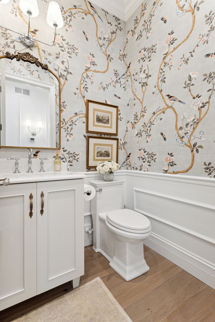 a white toilet sitting next to a sink in a bathroom under a mirror and framed pictures