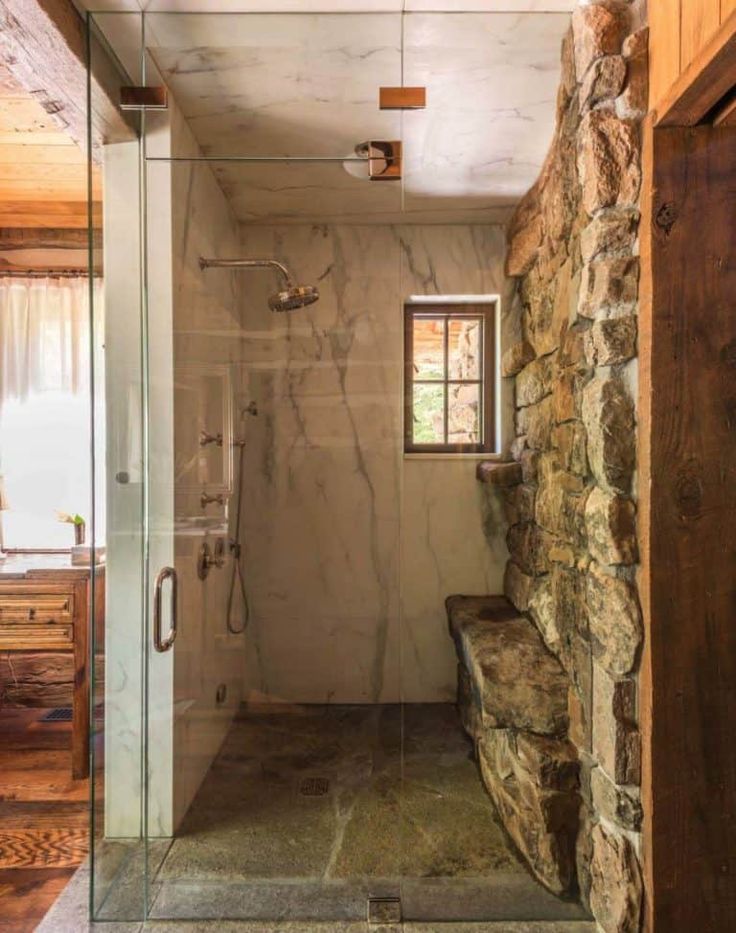 a bathroom with stone walls and a walk in shower next to a window on the wall