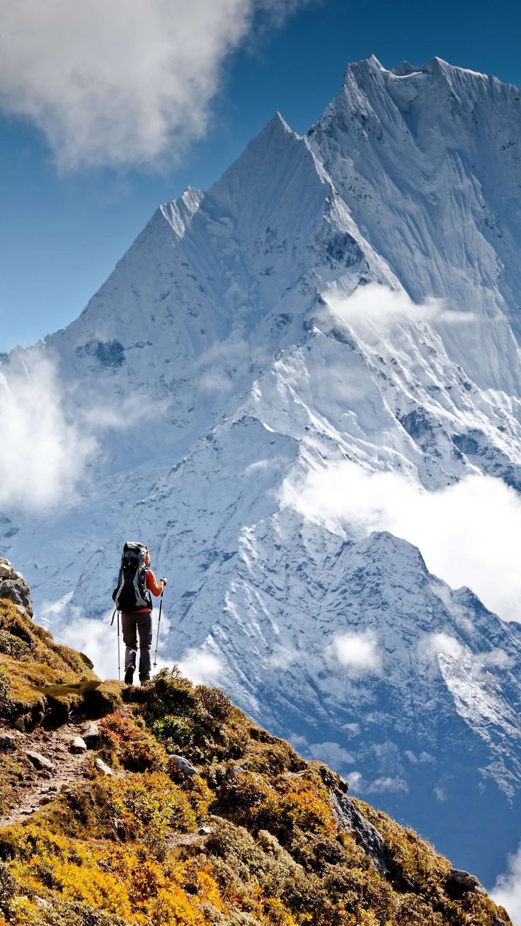 a man hiking up the side of a mountain with a large snow covered peak in the background