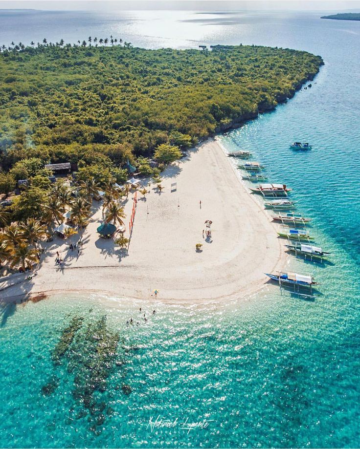 an aerial view of a beach with boats in the water and palm trees surrounding it