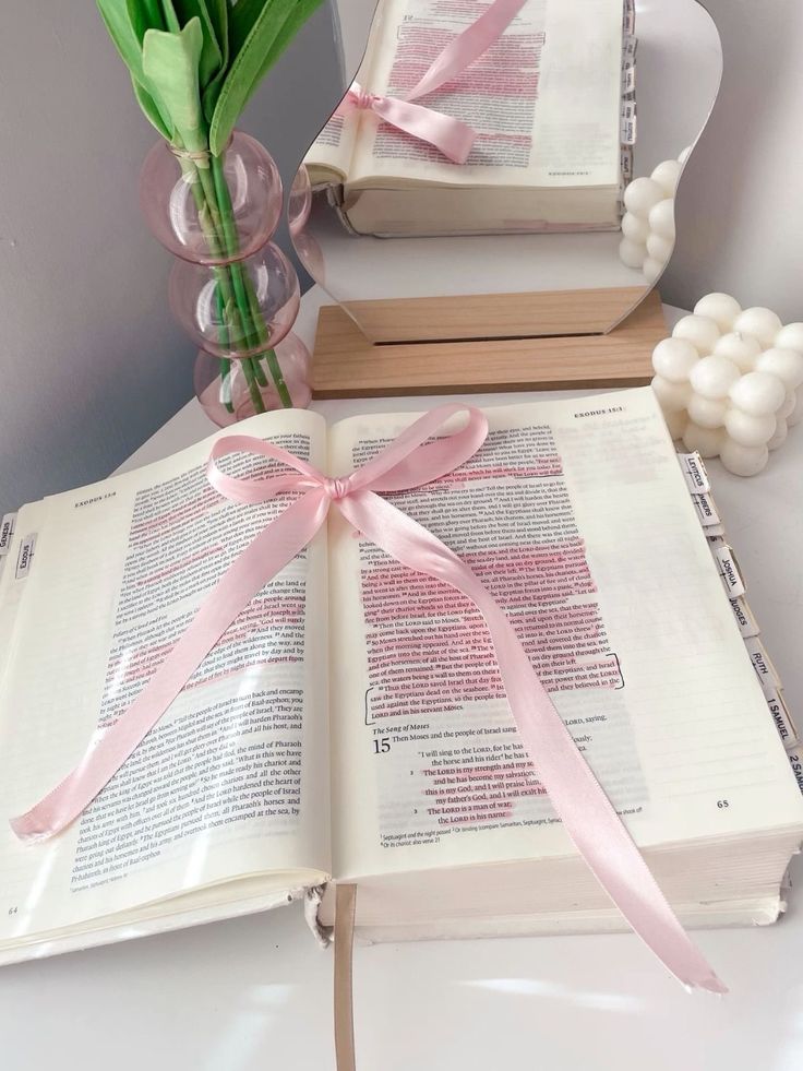 two open books with pink ribbon and flowers in vases on table next to them