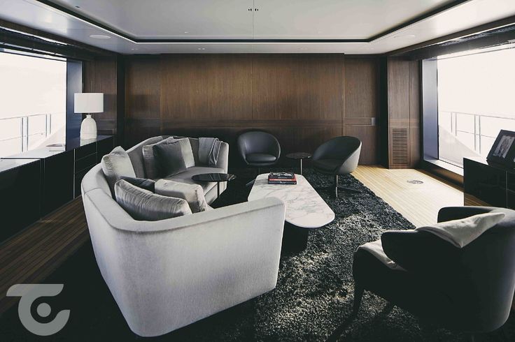 a living room filled with lots of furniture next to two large windows and a flat screen tv on top of a wooden wall