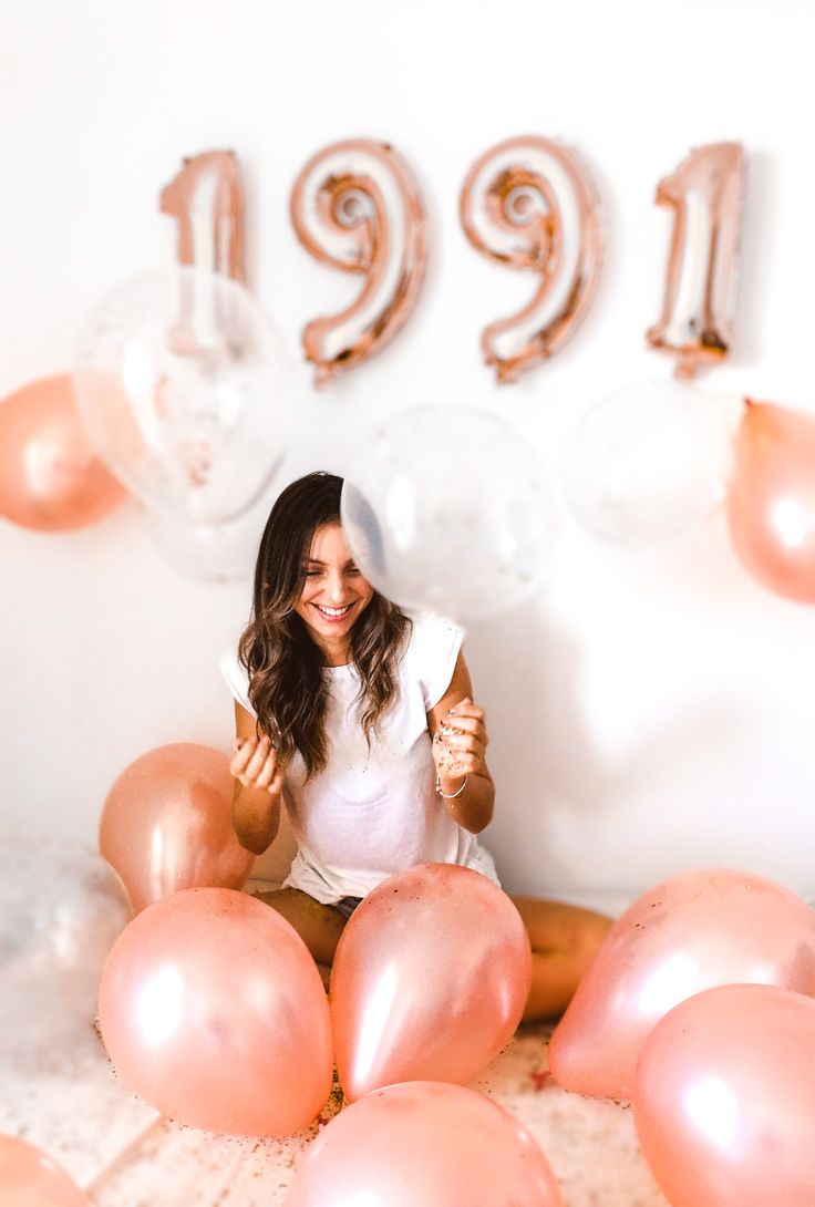 a woman sitting in front of balloons and giving the thumbs up sign with her thumb