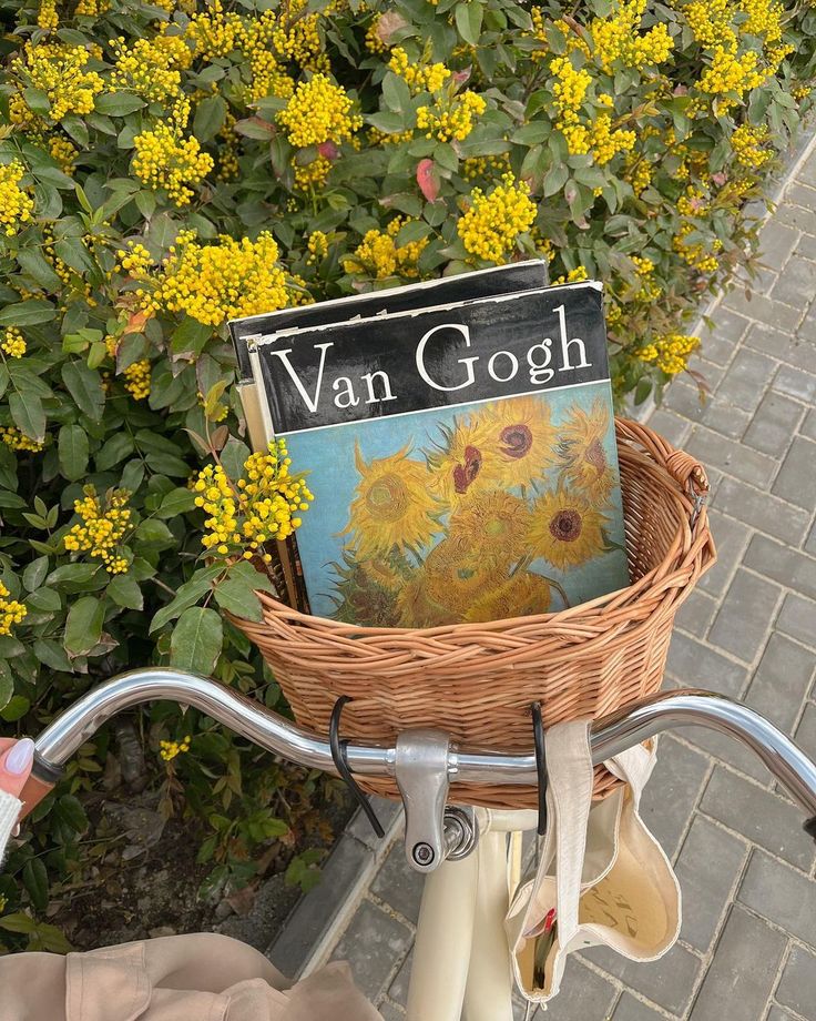 a bicycle with a basket full of books in front of some yellow flowers and bushes