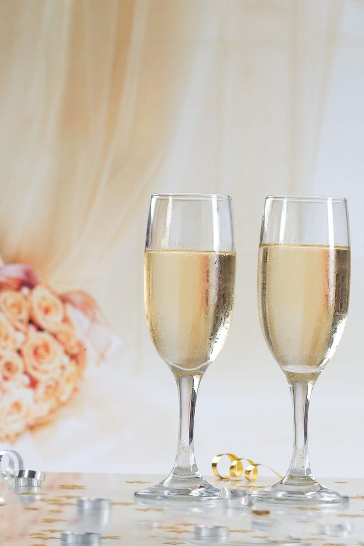 two champagne glasses sitting next to each other on a table with flowers in the background