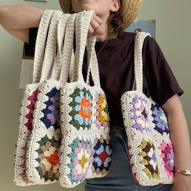 a woman holding four crocheted purses in front of her face and wearing a straw hat