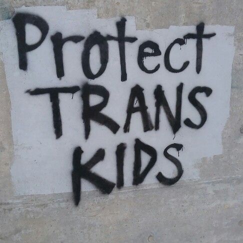 the words protect transs kids are spray painted on a white wall with black graffiti