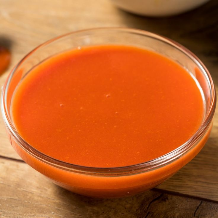 a glass bowl filled with red sauce on top of a wooden table