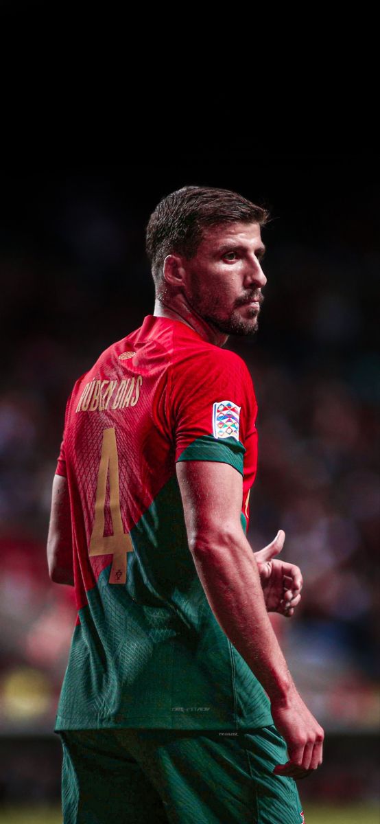 a soccer player in red and green uniform standing on the field with his hand out