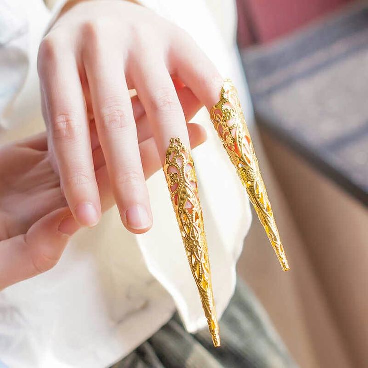 a woman holding two gold colored nails in her hand