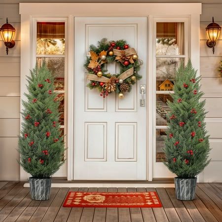 two christmas wreaths are on the front door of a house with potted trees