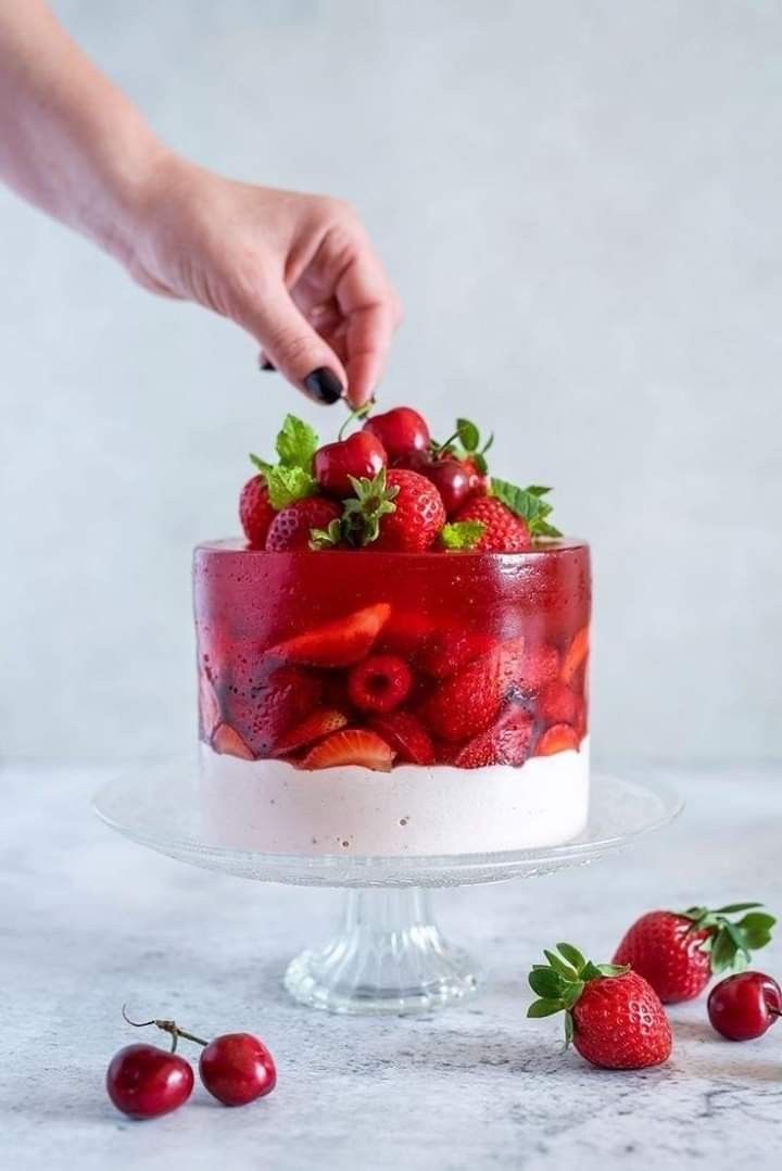 someone is decorating a cake with strawberries and cherries