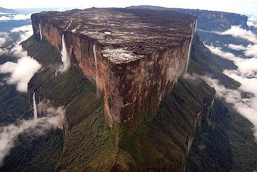 an aerial view of a mountain with clouds surrounding it and the edge of the cliff