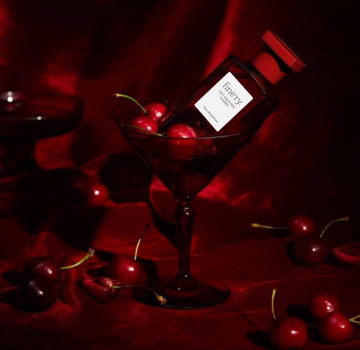 a glass filled with cherries sitting on top of a table next to a red cloth