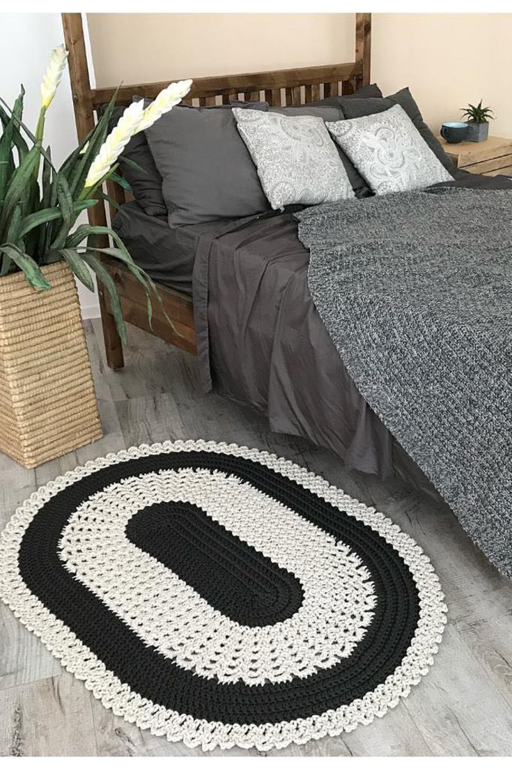 a black and white crocheted rug on the floor next to a wooden bed