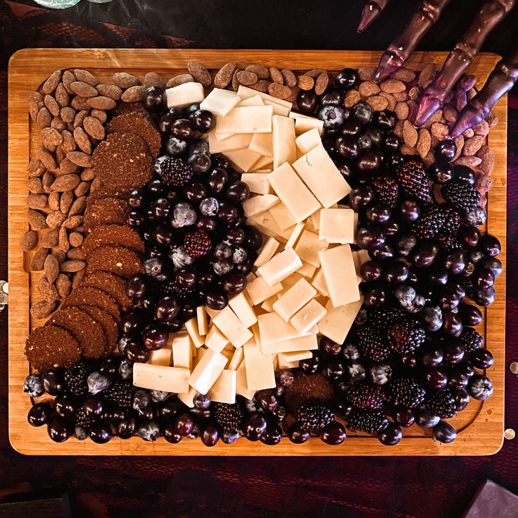 a wooden cutting board topped with lots of cheese and berries next to crackers on top of it