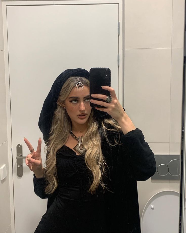 a woman taking a selfie in front of a bathroom mirror wearing a black hoodie