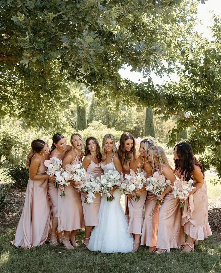 a group of women standing next to each other in front of trees and bushes holding bouquets