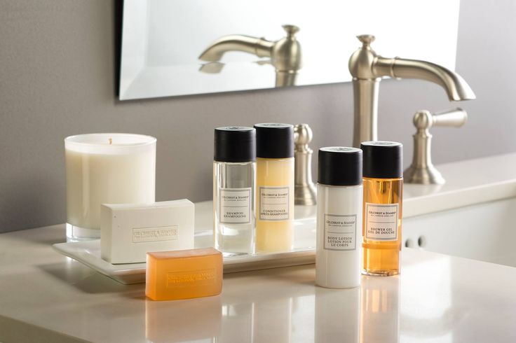 a bathroom counter with three bottles and soaps on it next to a candle in front of a mirror