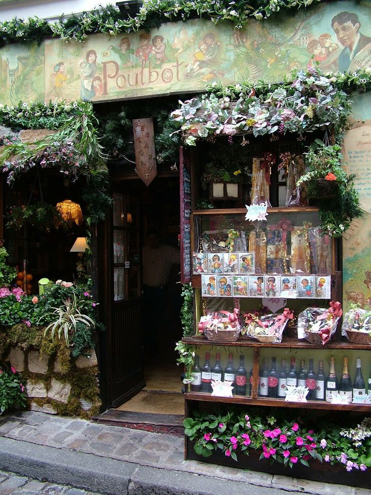 a flower shop with lots of flowers and plants on the outside wall, in front of a building