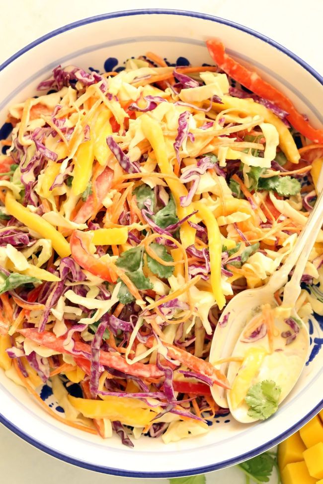 a colorful salad in a blue and white bowl with a wooden spoon on the side