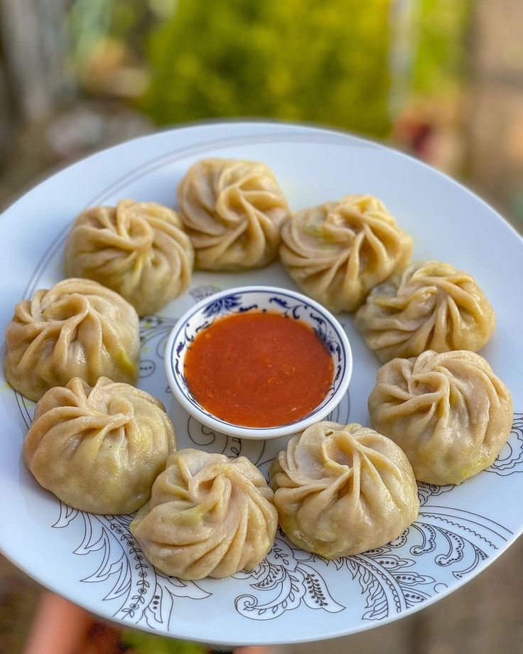 a person holding a plate with dumplings on it and dipping sauce in the middle