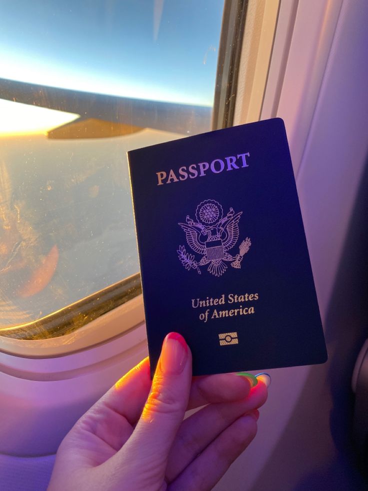 a person holding up a passport in front of an airplane window