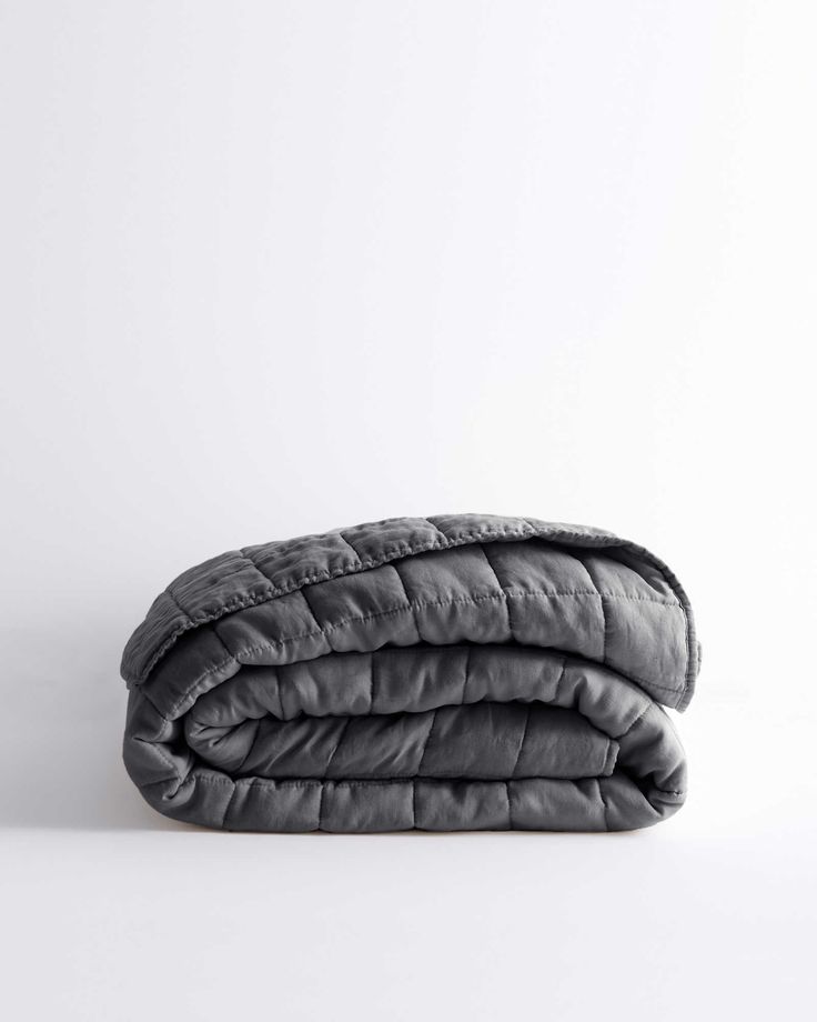 the grey quilted blanket is folded on top of each other, with one side rolled up