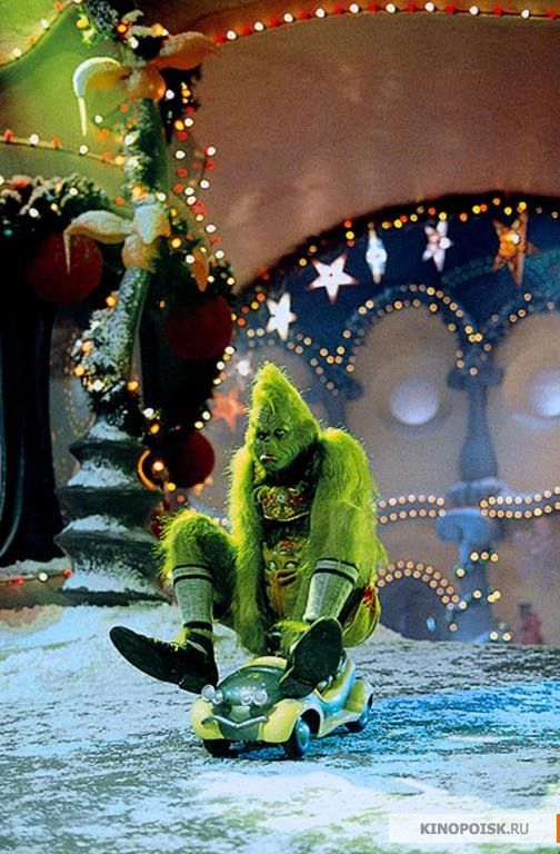 a man dressed as a creature sitting on top of a skateboard in front of a christmas tree