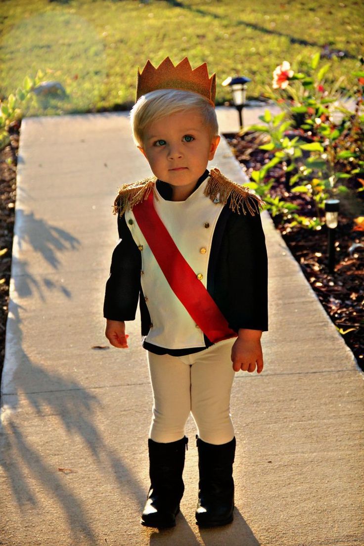 a little boy wearing a crown and standing on a sidewalk with his hands in his pockets