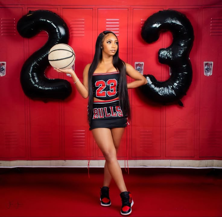 a woman standing in front of lockers holding a basketball ball and number 23 balloon