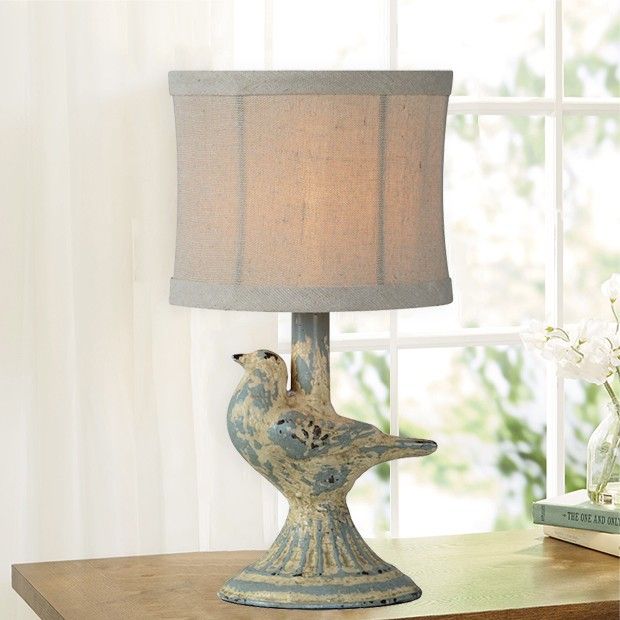 a bird lamp sitting on top of a wooden table next to a vase with flowers