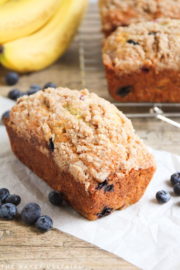 two blueberry muffins sitting on top of paper next to bananas and some other fruit