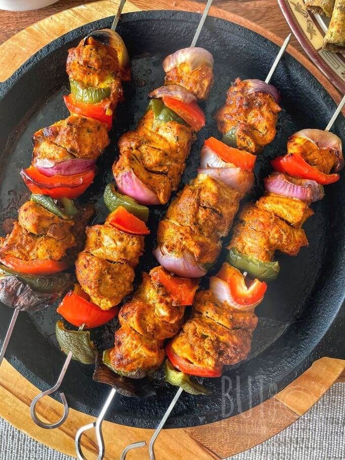 several skewers filled with meat and veggies on top of a black plate