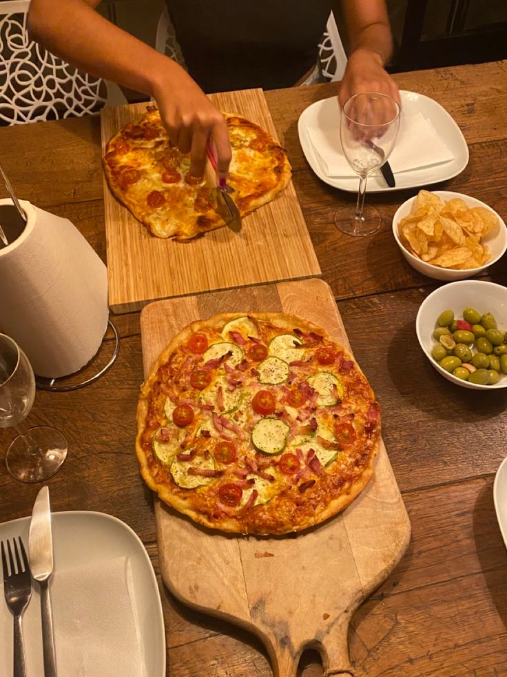 a pizza sitting on top of a wooden cutting board next to bowls of olives