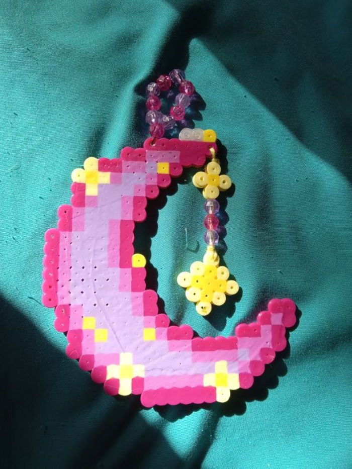 a pink and yellow beaded letter on a green cloth with beads hanging from it