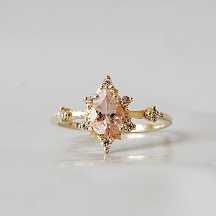 an engagement ring with a pink diamond and two white diamonds on the side, set in yellow gold