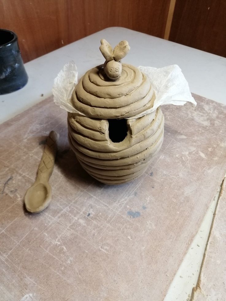 a wooden spoon sitting on top of a table next to a clay pot with a bird in it