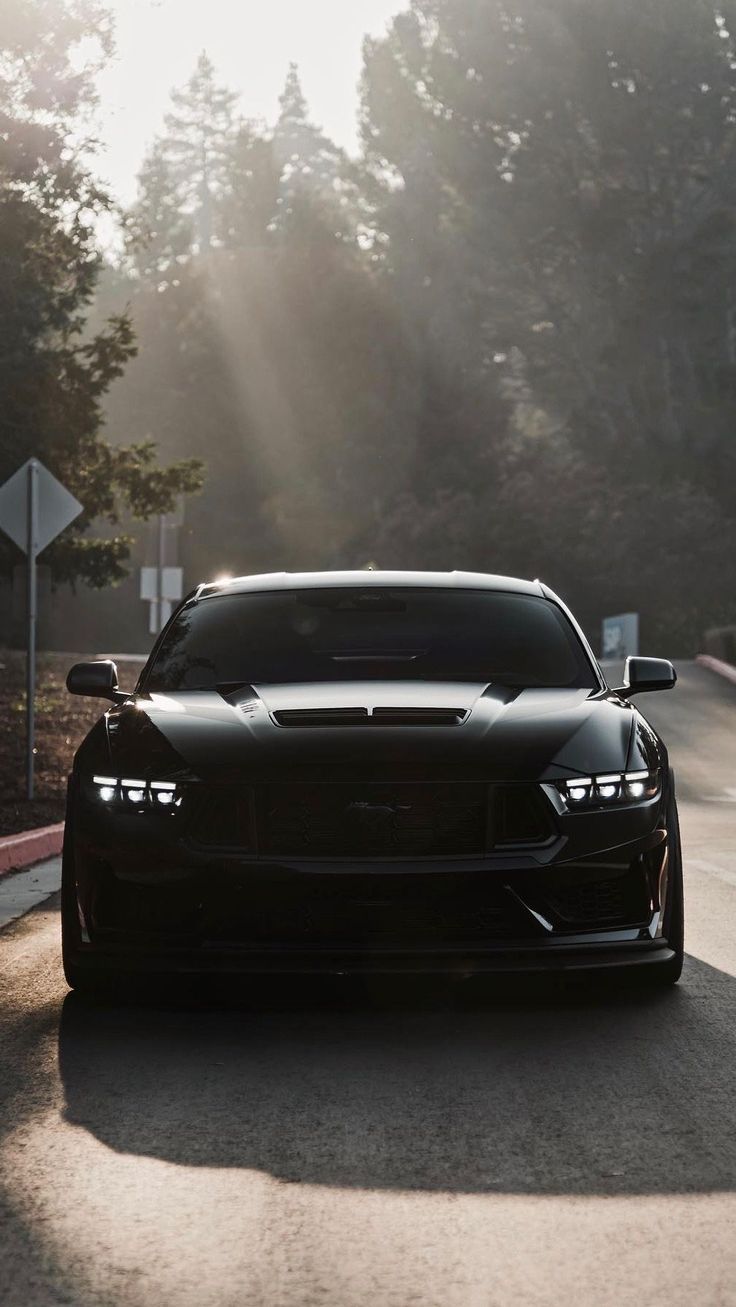 the front end of a black sports car driving on a road with trees in the background