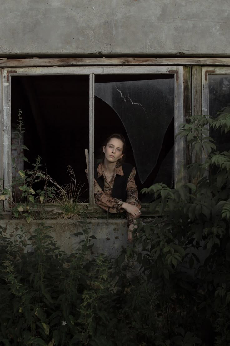 a woman sitting in the window of an abandoned building with her arms crossed and looking out