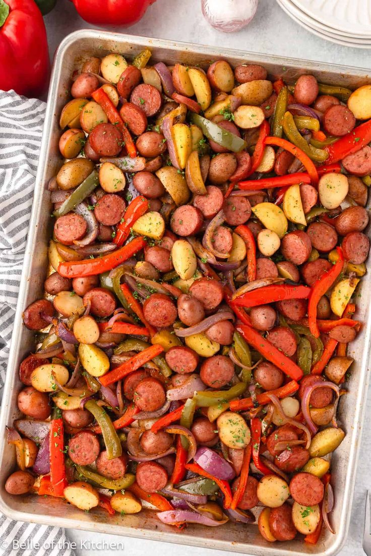 a casserole dish filled with sausages, potatoes and peppers next to tomatoes