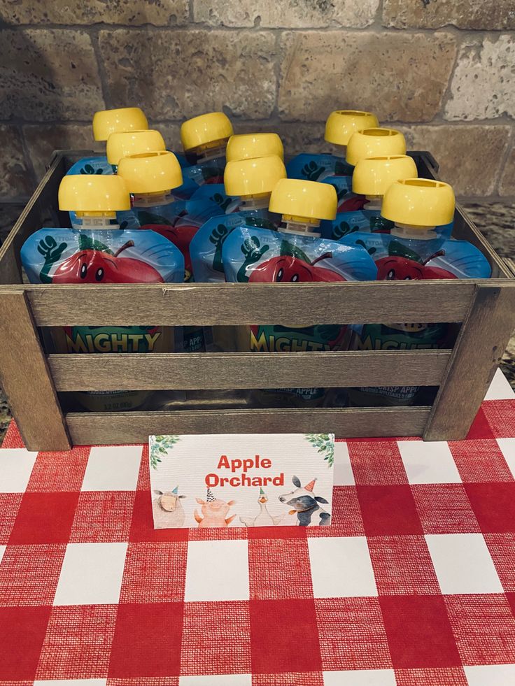 a wooden crate filled with apple cider bottles sitting on top of a red and white checkered table cloth